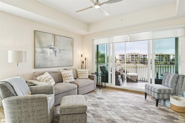 living room with ceiling fan, a tray ceiling, and wood finished floors