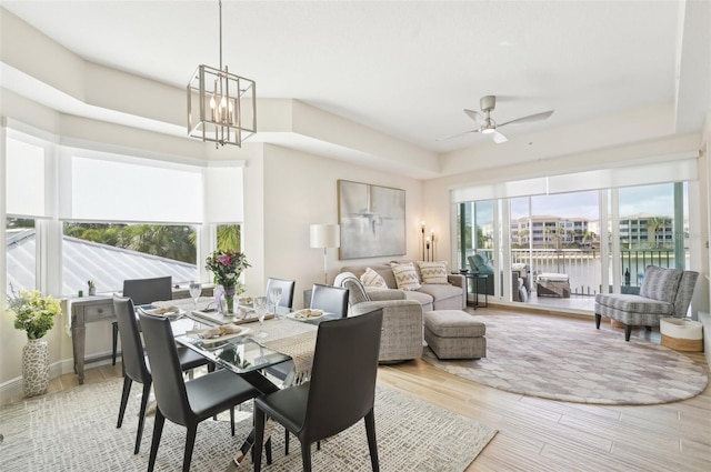 dining space with a tray ceiling, wood finished floors, and ceiling fan with notable chandelier