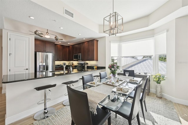 dining room featuring visible vents, light wood-type flooring, a raised ceiling, recessed lighting, and baseboards