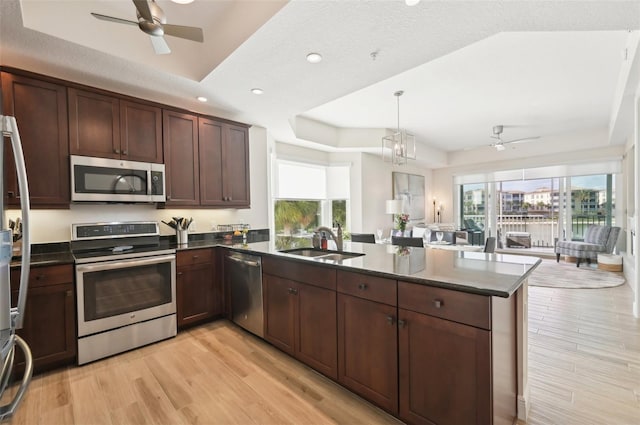 kitchen featuring light wood-style flooring, a sink, appliances with stainless steel finishes, a peninsula, and a raised ceiling