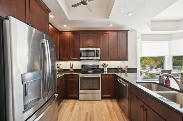 kitchen featuring a tray ceiling, light wood-style flooring, recessed lighting, a sink, and appliances with stainless steel finishes