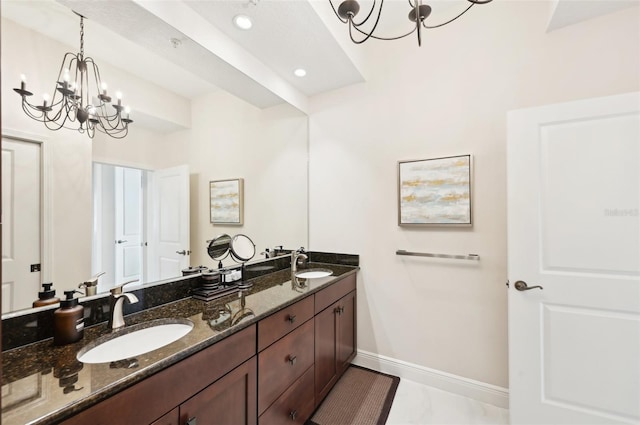 full bath with a sink, baseboards, an inviting chandelier, and double vanity