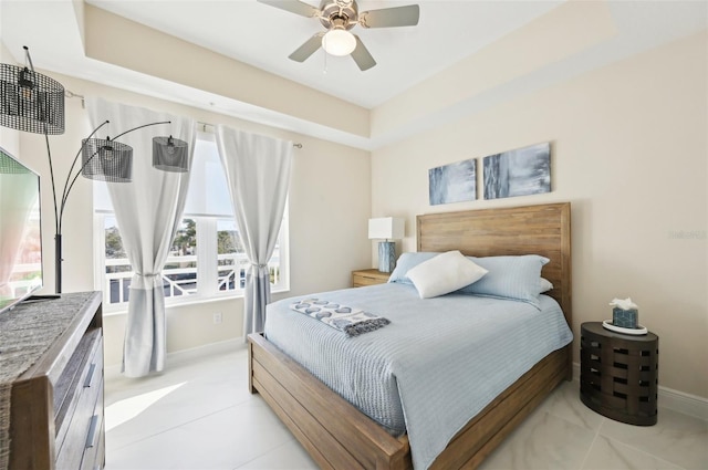 bedroom featuring ceiling fan, a tray ceiling, and baseboards