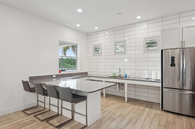 kitchen featuring light wood finished floors, a peninsula, a sink, stainless steel refrigerator, and tasteful backsplash