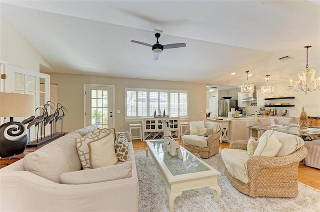 living area featuring visible vents, ceiling fan with notable chandelier, light wood-style floors, and lofted ceiling