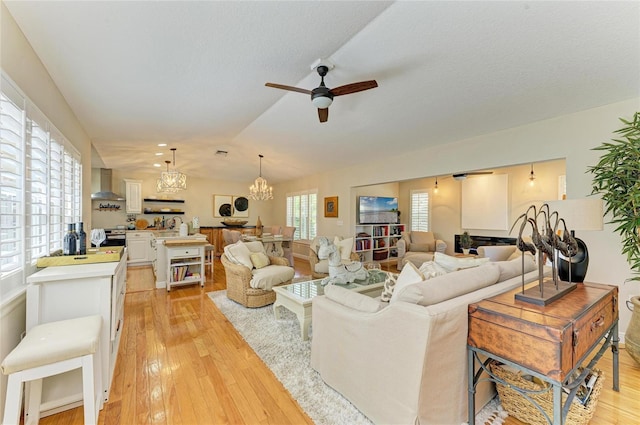 living area featuring light wood-style flooring, vaulted ceiling, and ceiling fan with notable chandelier