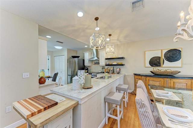 kitchen with visible vents, an inviting chandelier, freestanding refrigerator, a sink, and wall chimney exhaust hood