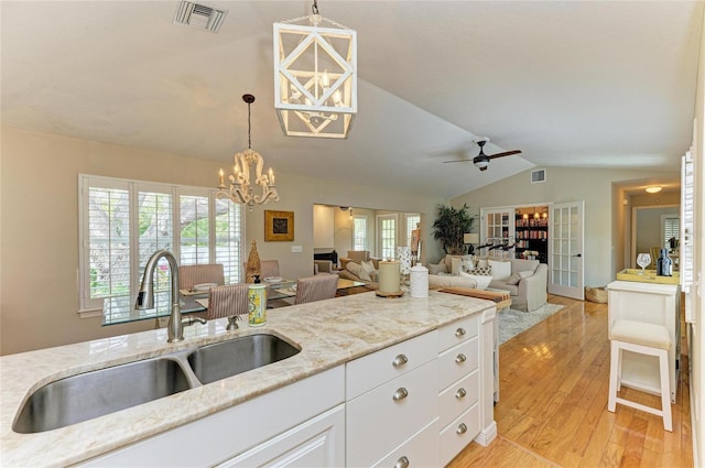 kitchen with light wood finished floors, visible vents, lofted ceiling, light stone counters, and a sink