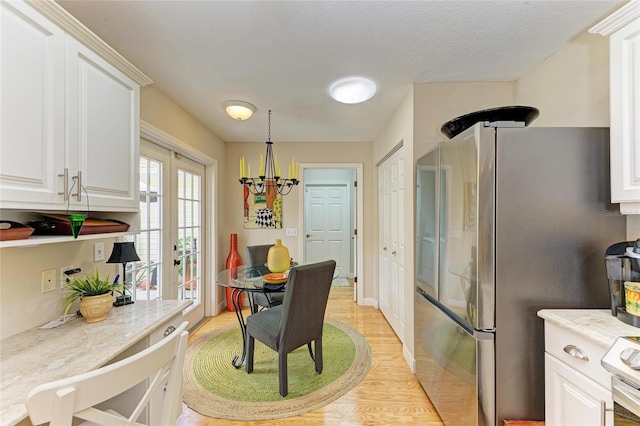 kitchen featuring a textured ceiling, stainless steel appliances, an inviting chandelier, white cabinets, and light wood finished floors