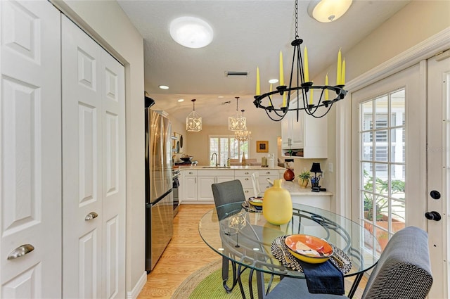 dining space with visible vents, light wood-style floors, and an inviting chandelier