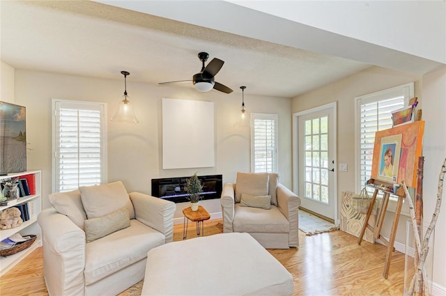 living room featuring a glass covered fireplace, ceiling fan, baseboards, and light wood-style floors