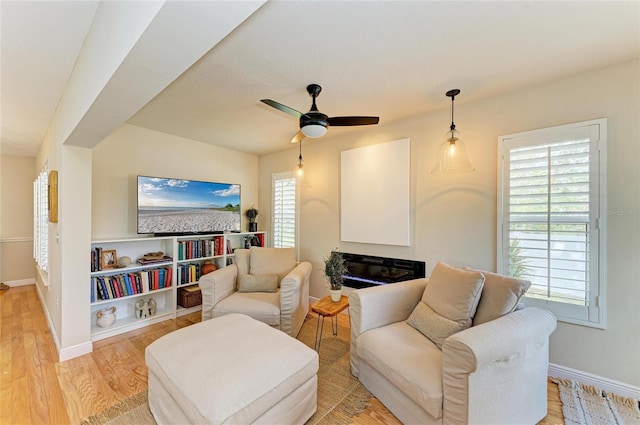 living room featuring a glass covered fireplace, baseboards, light wood-style flooring, and a ceiling fan