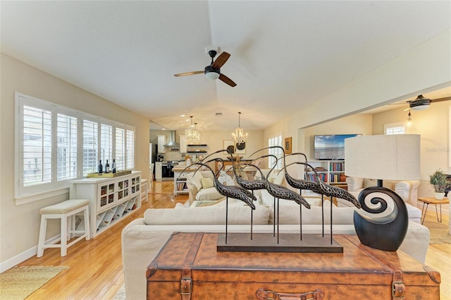 living area featuring light wood-style floors, a healthy amount of sunlight, vaulted ceiling, and ceiling fan with notable chandelier