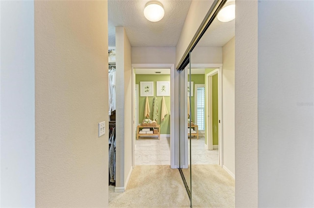 hall featuring light colored carpet, baseboards, a textured wall, and a textured ceiling