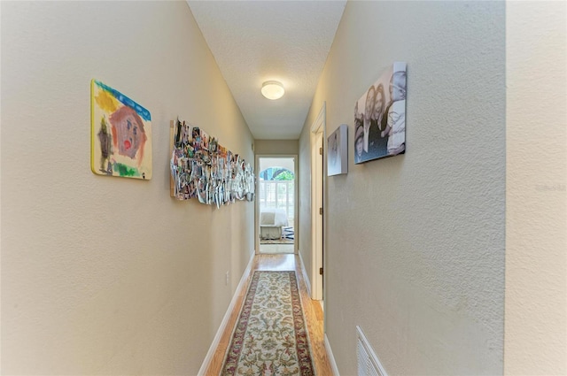 hallway with visible vents, baseboards, a textured ceiling, and a textured wall