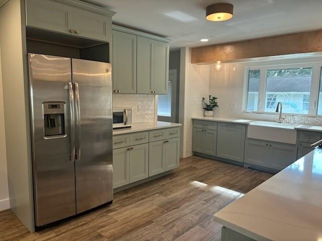 kitchen featuring a sink, tasteful backsplash, wood finished floors, appliances with stainless steel finishes, and light countertops