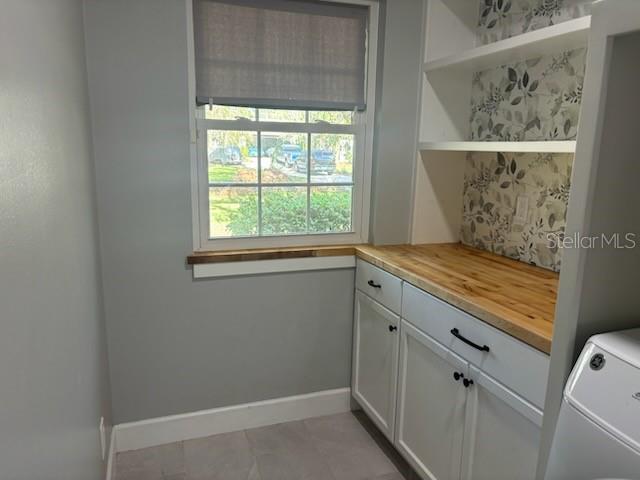 interior space with light tile patterned floors, baseboards, cabinet space, and washer / dryer