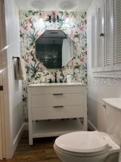 half bathroom with toilet, wood finished floors, vanity, and wallpapered walls