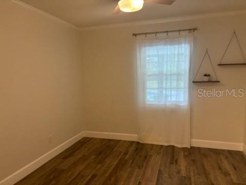 spare room featuring dark wood finished floors, crown molding, and baseboards