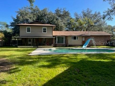 rear view of property with an outdoor pool and a lawn