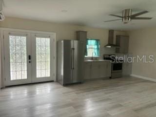 kitchen featuring baseboards, wall chimney range hood, french doors, stainless steel appliances, and a ceiling fan