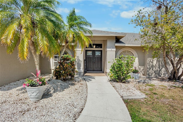 view of exterior entry with stucco siding and a shingled roof