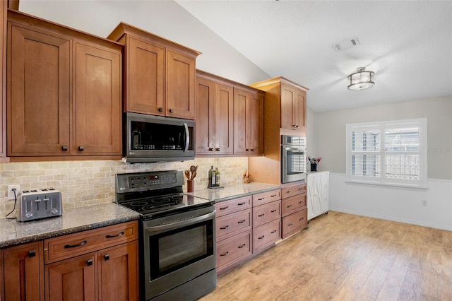 kitchen featuring brown cabinetry, light wood finished floors, lofted ceiling, dark stone counters, and stainless steel appliances