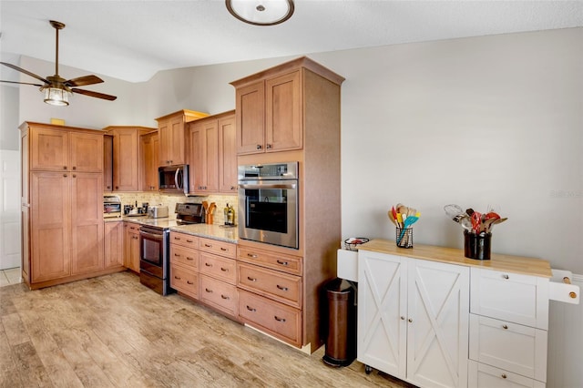 kitchen featuring ceiling fan, decorative backsplash, vaulted ceiling, stainless steel appliances, and light wood-type flooring