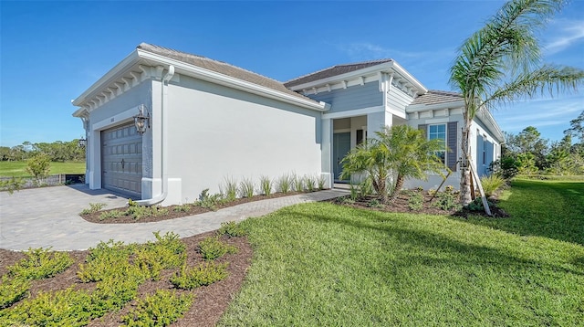 view of front of property featuring decorative driveway, a front lawn, an attached garage, and stucco siding