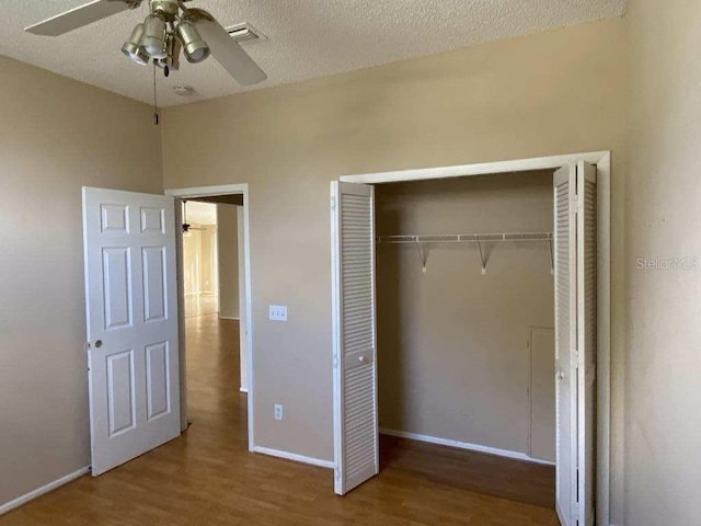 unfurnished bedroom with wood finished floors, baseboards, visible vents, a closet, and a textured ceiling