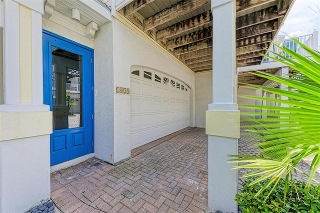 view of exterior entry with stucco siding, decorative driveway, and a garage