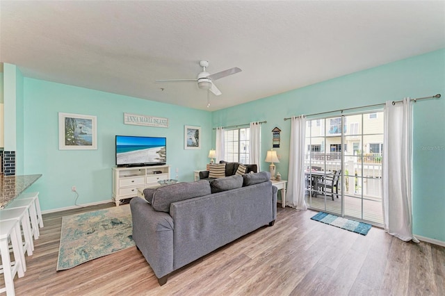 living area with baseboards, wood finished floors, and a ceiling fan