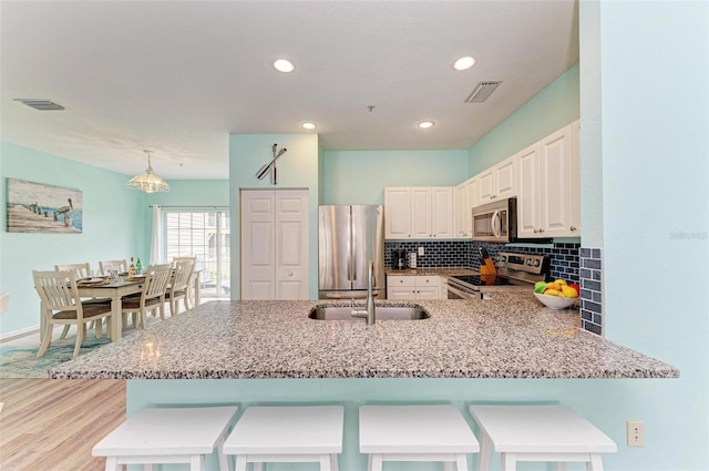 kitchen with a sink, visible vents, light stone counters, and appliances with stainless steel finishes