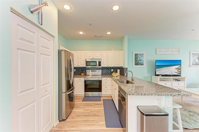 kitchen with light stone countertops, a kitchen bar, appliances with stainless steel finishes, a peninsula, and a sink