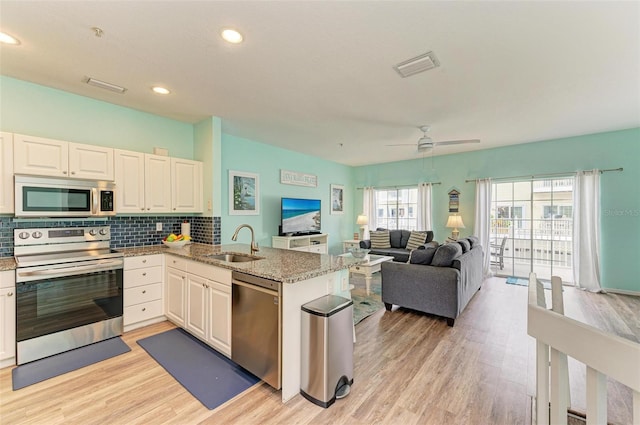 kitchen featuring visible vents, a peninsula, a sink, appliances with stainless steel finishes, and tasteful backsplash