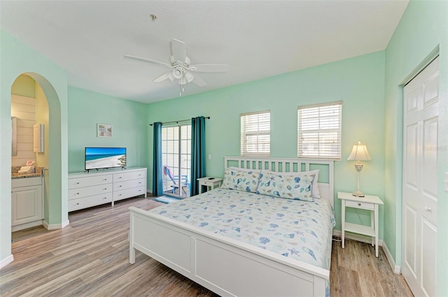 bedroom featuring arched walkways, baseboards, light wood-style floors, and a ceiling fan