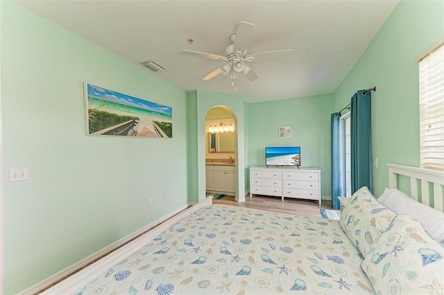 bedroom featuring visible vents, ensuite bathroom, wood finished floors, arched walkways, and baseboards