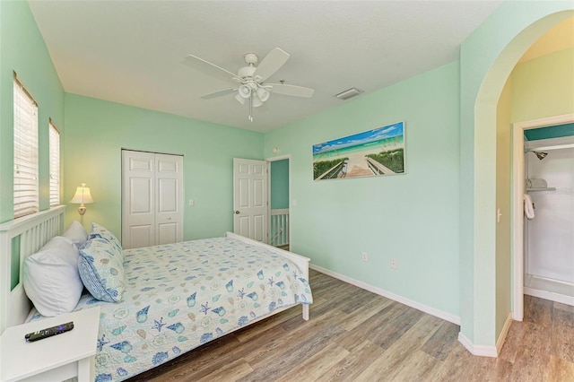 bedroom featuring visible vents, baseboards, arched walkways, wood finished floors, and a closet