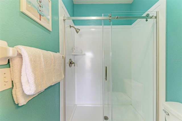 full bath with toilet, a shower stall, and a textured wall