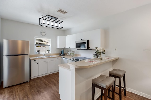 kitchen featuring visible vents, dark wood finished floors, a peninsula, stainless steel appliances, and a sink