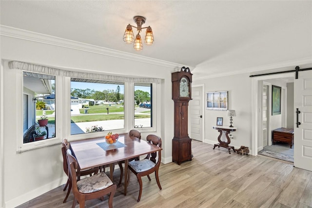 dining area with crown molding, baseboards, light wood-style floors, and a barn door