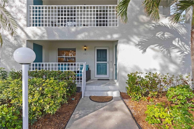 view of exterior entry featuring stucco siding, a balcony, and covered porch