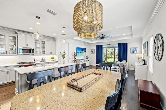 dining area with visible vents, crown molding, ceiling fan with notable chandelier, dark wood-style floors, and a raised ceiling