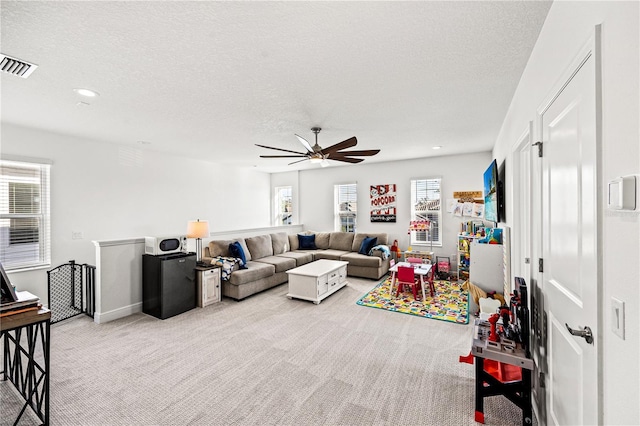 living room with a ceiling fan, plenty of natural light, light colored carpet, and visible vents