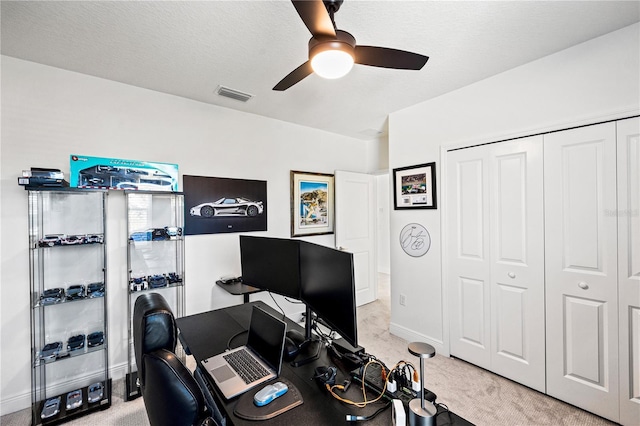 office featuring visible vents, baseboards, light carpet, a textured ceiling, and a ceiling fan