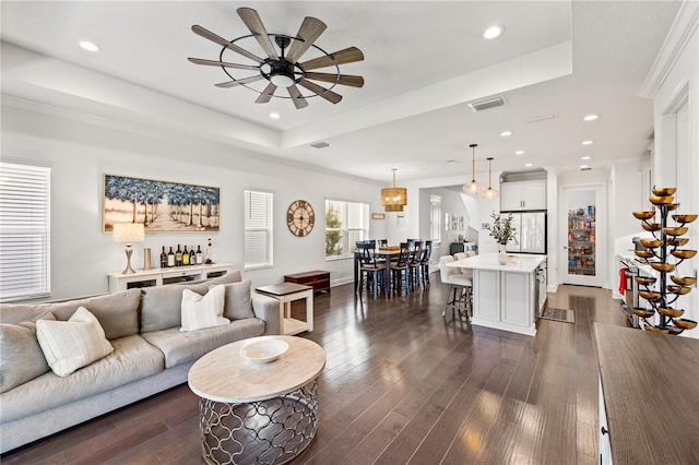 living room with a tray ceiling, visible vents, a ceiling fan, and dark wood-style floors