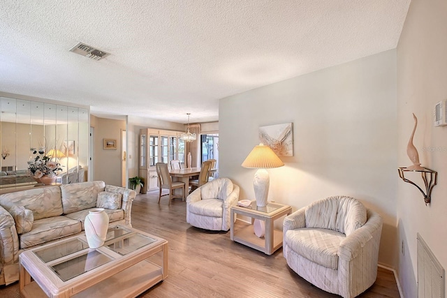 living room with visible vents, a textured ceiling, an inviting chandelier, and wood finished floors