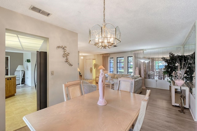 dining area featuring a notable chandelier, visible vents, light wood finished floors, and a textured ceiling