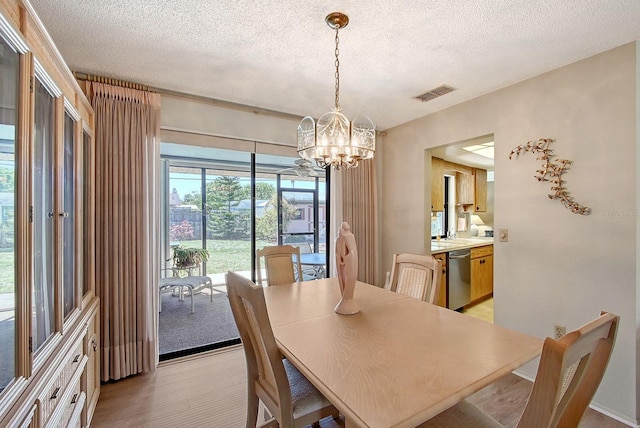 dining space with an inviting chandelier, visible vents, light wood finished floors, and a textured ceiling