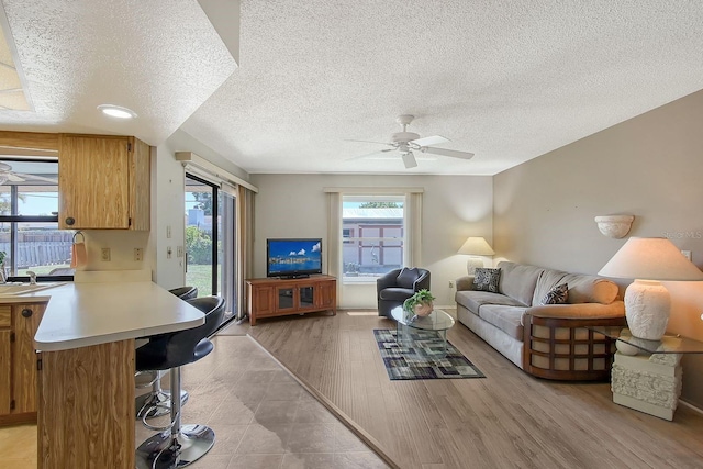 living room featuring light wood-style floors, a ceiling fan, and a textured ceiling